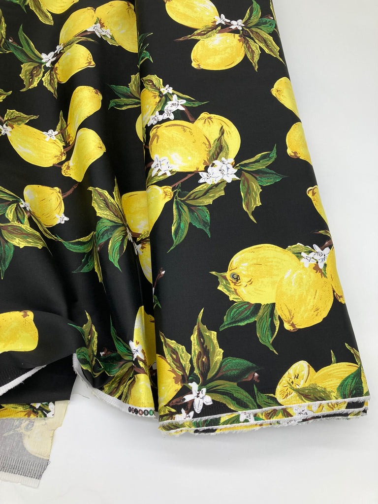 The fabric shown on a bolt. It has bright yellow lemons with lemon blossom and leaves, set against a black background.