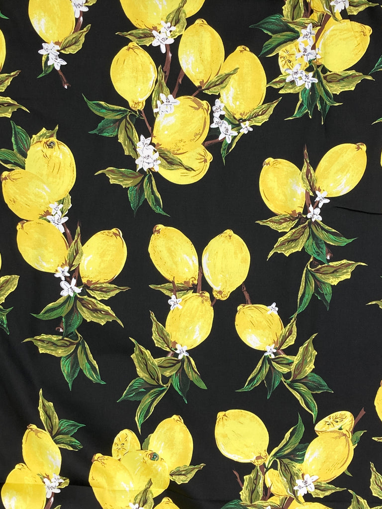 A picture of the fabric shown flat. The fabric shown on a bolt. It has groups of lemons with lemon blossom and leaves, set against a black background.